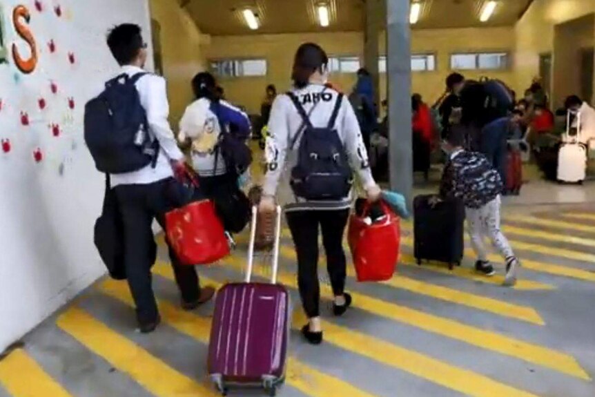 A group of adults and children wheel suitcases into a building.