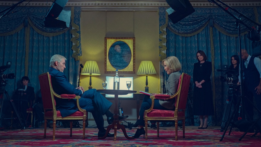 Two people, a man and a woman, sit in an ornate room 