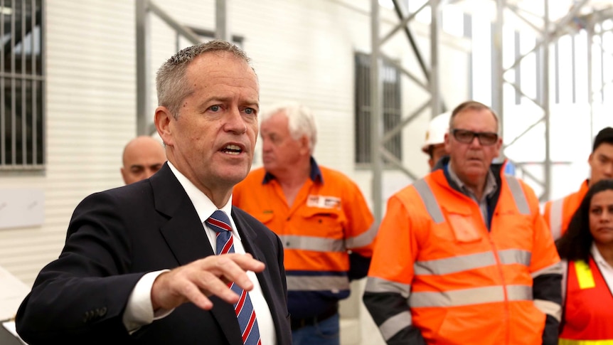 Bill Shorten points as he talks to a group of workers in high-vis gear