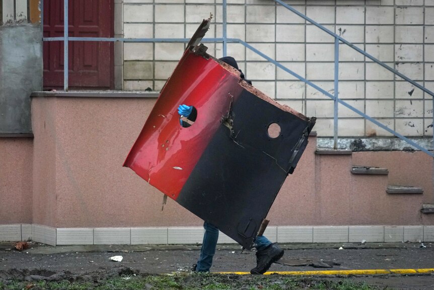A person carrying a large door fragment of debris after a crash