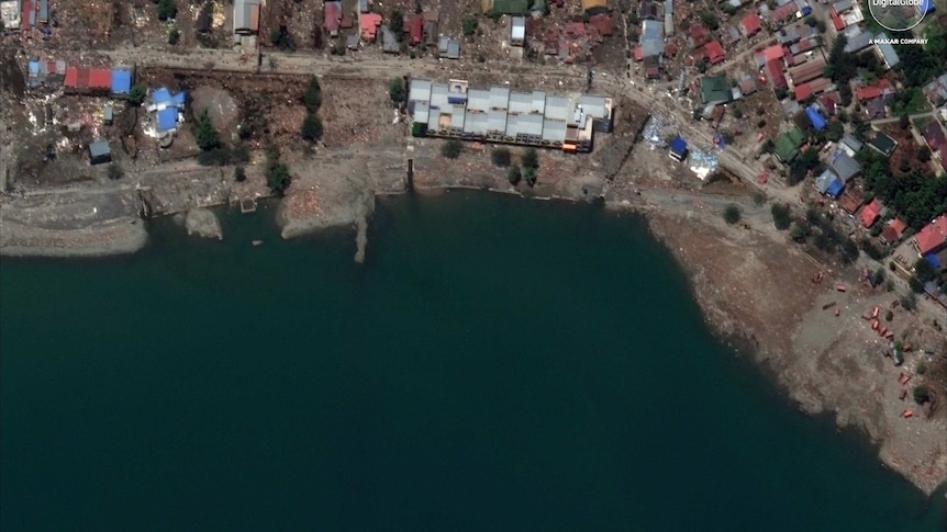 Sattelite image shows rubble on the shore of Palu, and no jetty in the water. Many buildings are destroyed.