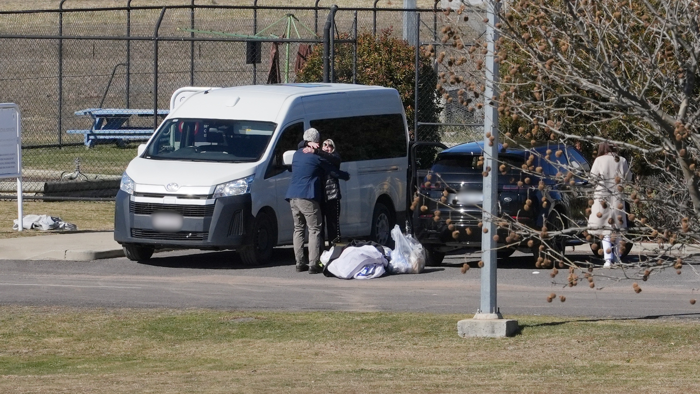 People in the distance near a van on the other side of a fence.