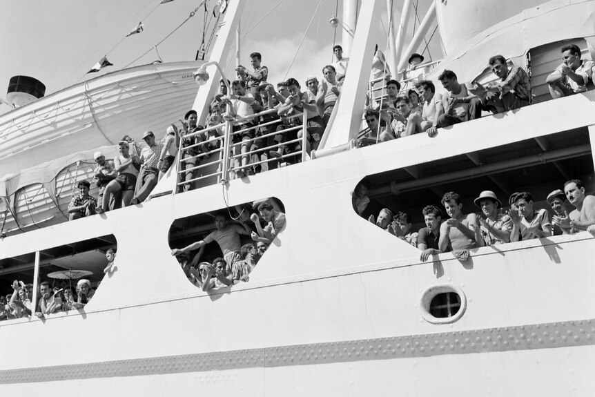 A 1950s black and white photo of a crowded ship arriving.