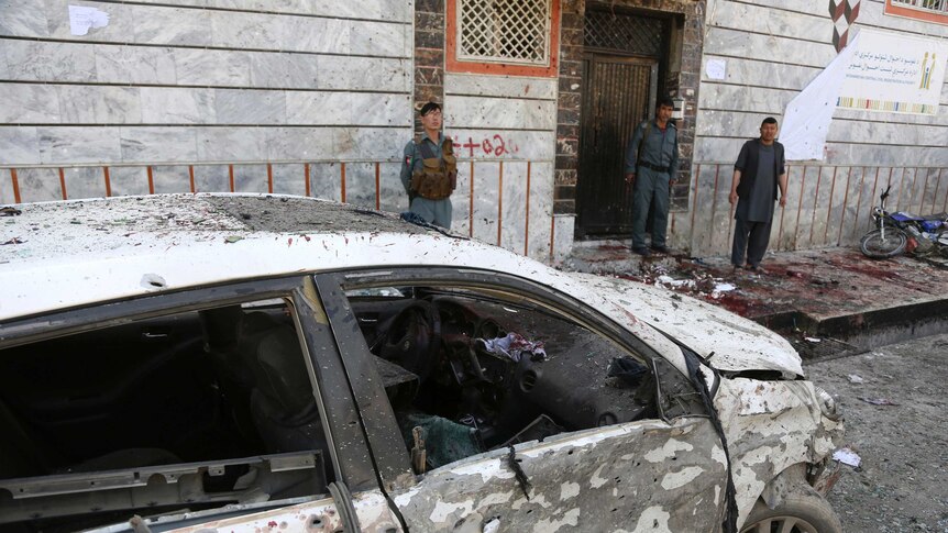 A damaged car and blood on the street are seen outside the voter registration centre guarded by security personnel.