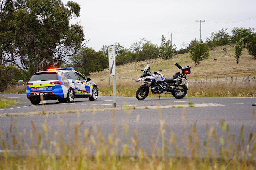 A police car and a police motorbike stopped at a T-junction with lights flashing