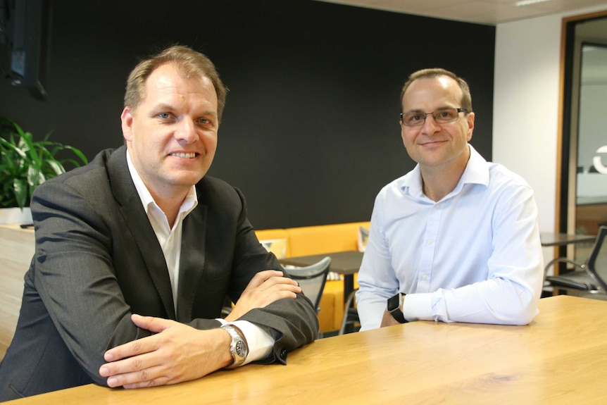 Zaun Bhana, right, sits alongside Adam Soudure in an office as both smile for a photo.