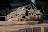 A man in a military uniform rests his head on a pile of boxes