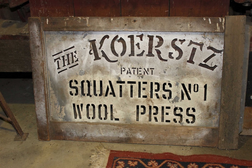 An old wool press sign leans against the wool press