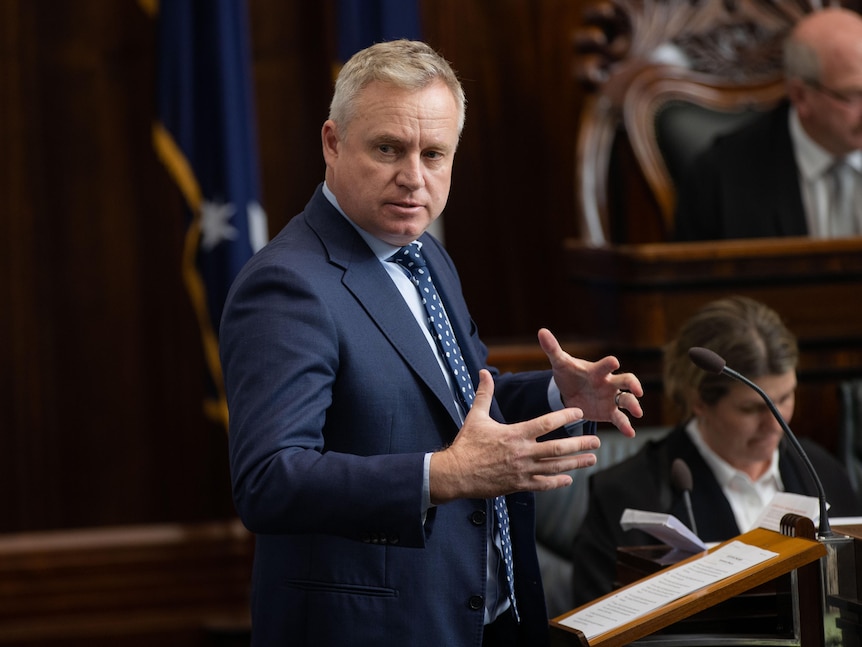 A man in a suit uses his hands as he addresses Parliament.