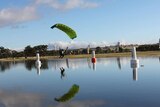 A skydiver with a green parachute travels over water preparing to land.