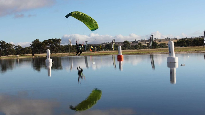 A skydiver with a green parachute travels over water preparing to land.