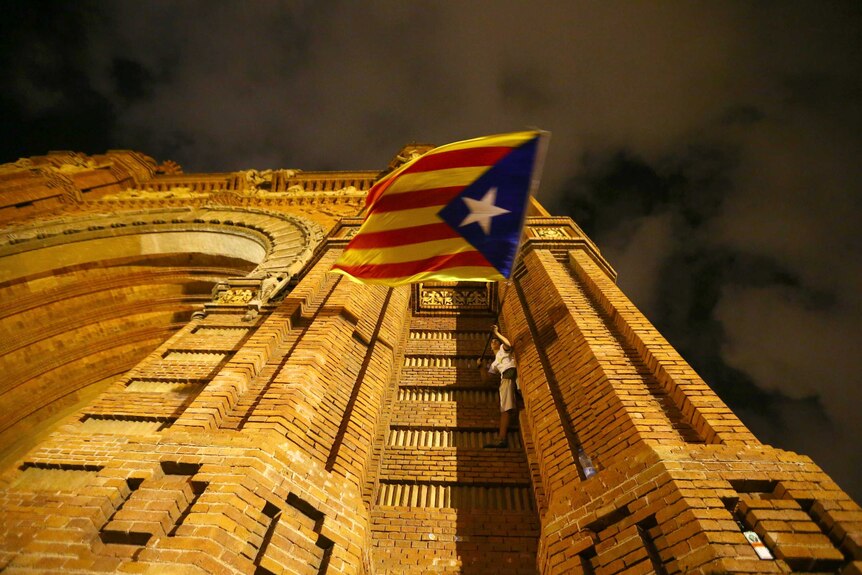 A man waves a separatist Catalonian flag while standing on the side of a building.