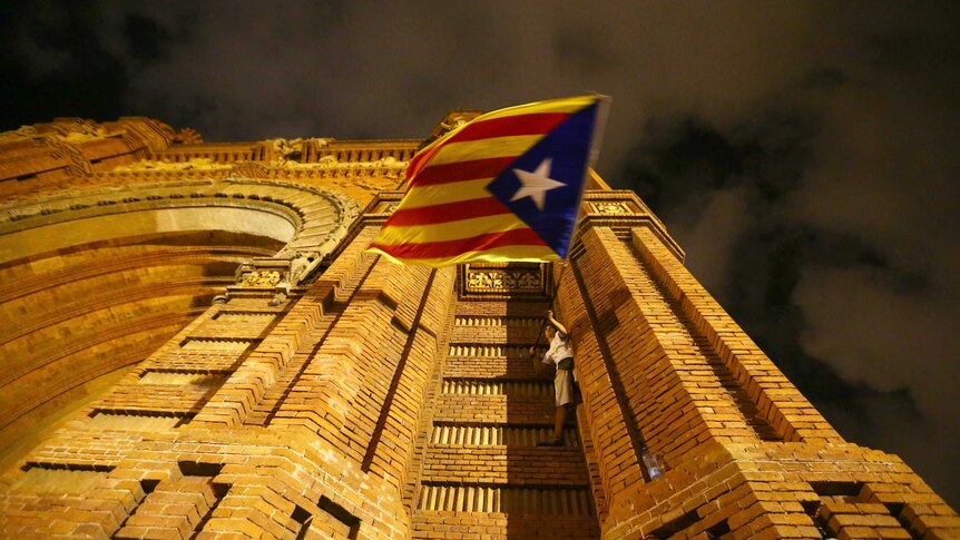 A man waves a separatist Catalonian flag while standing on the side of a building.