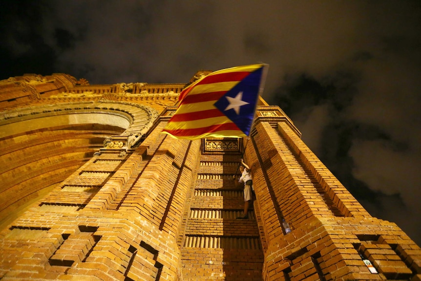 A man waves a separatist Catalonian flag while standing on the side of a building.