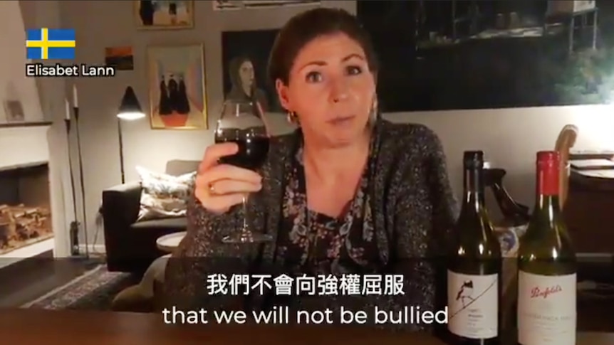 You view a screenshot of a woman holding a glass of red wine on a table with two bottles of Australian wine.