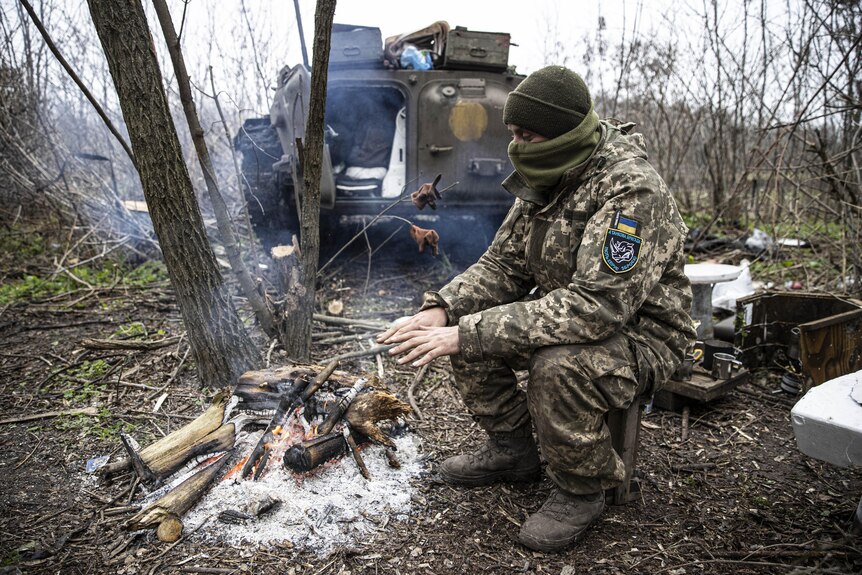 A soldier warms up in front of woodfire. 