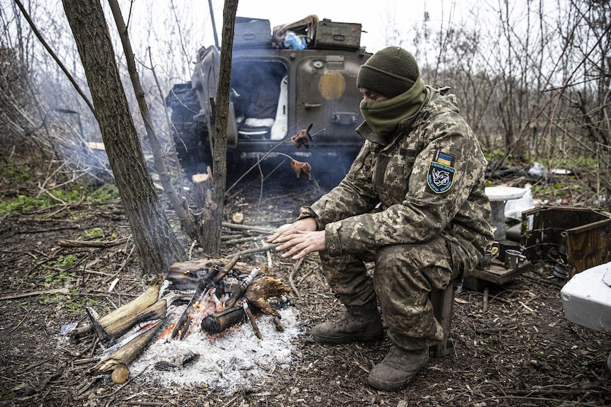 A soldier warms up in front of woodfire. 