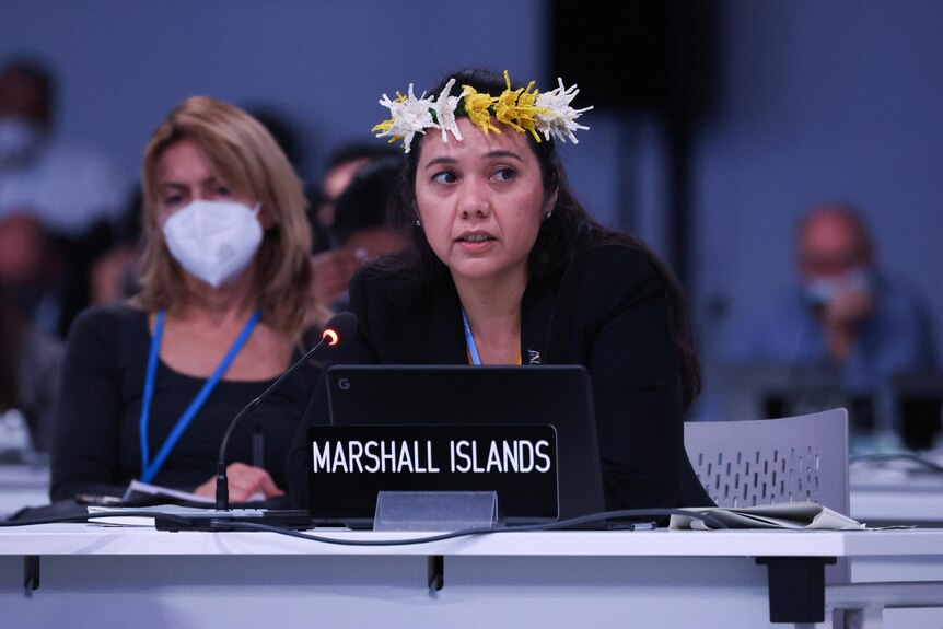 A woman in a floral headdress sits at a table in a conference centre.