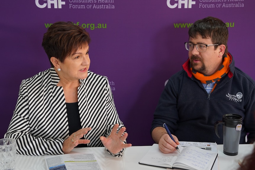 A woman sitting at a table with a man in front of a purple background