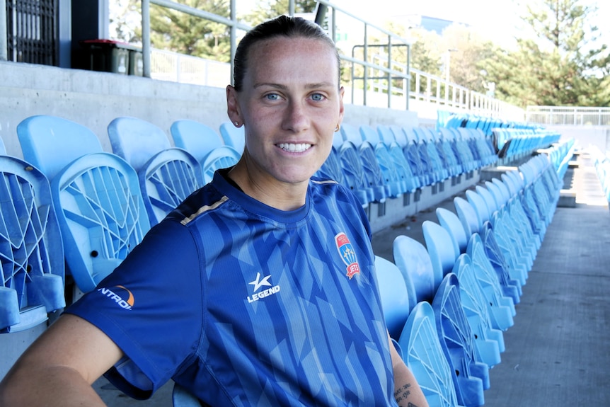 Soccer player Emily Van Egmond in her Newcastle Jets training jersey. She is sitting in the grandstand of the oval.