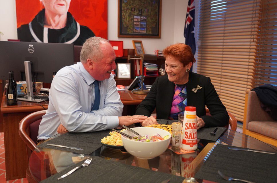 Pauline Hanson y Banarby Joyce sonríen con platos llenos de comida en una mesa de la oficina