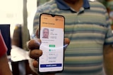 A man wearing a polo shirt in a pub lifts his phone displaying a driver license app.