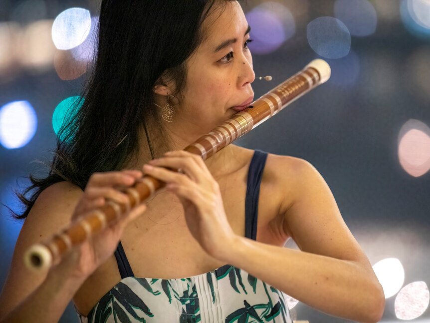 Chloe Chung blows into the mouthpiece of the bamboo dizi and holds the flute across the fingerholes as she plays