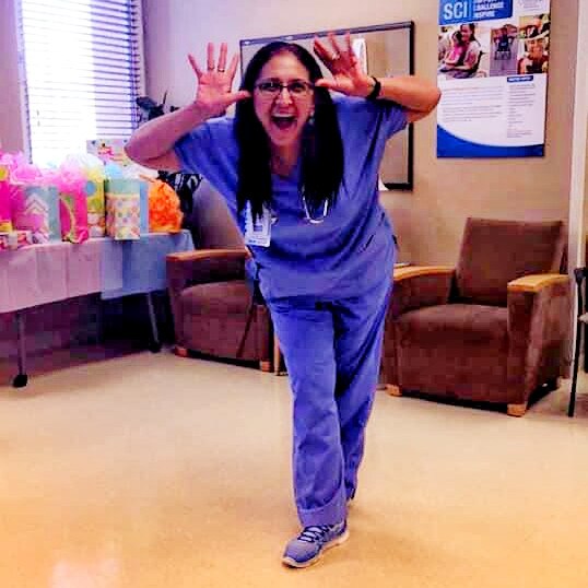 A woman in blue scrubs smiling and waving her hands