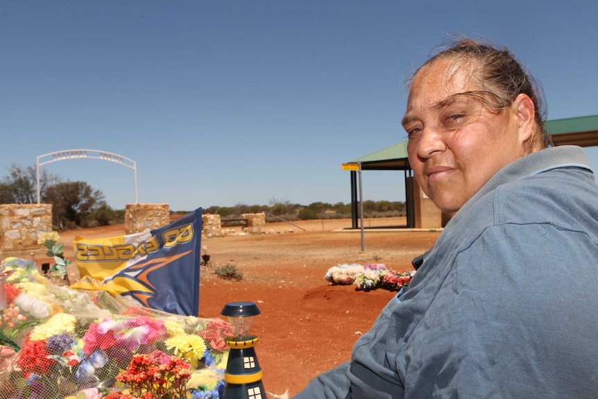 A woman sitting in a rural cemetery surrounded by flowers