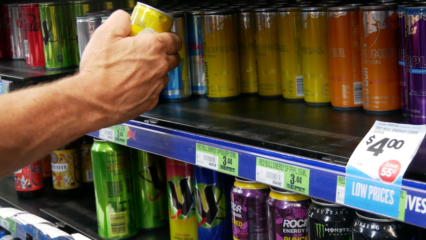 A hand reaches for energy drinks on a shelf