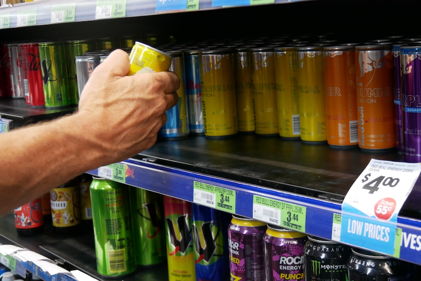 A hand reaches for energy drinks on a shelf