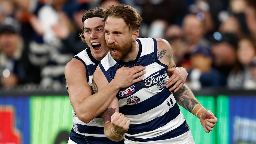 Two Geelong AFL players shout in celebration as they run back to the centre after kicking a goal.