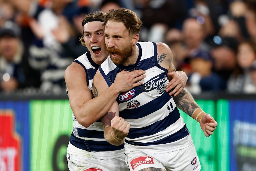 Two Geelong AFL players shout in celebration as they run back to the centre after kicking a goal.