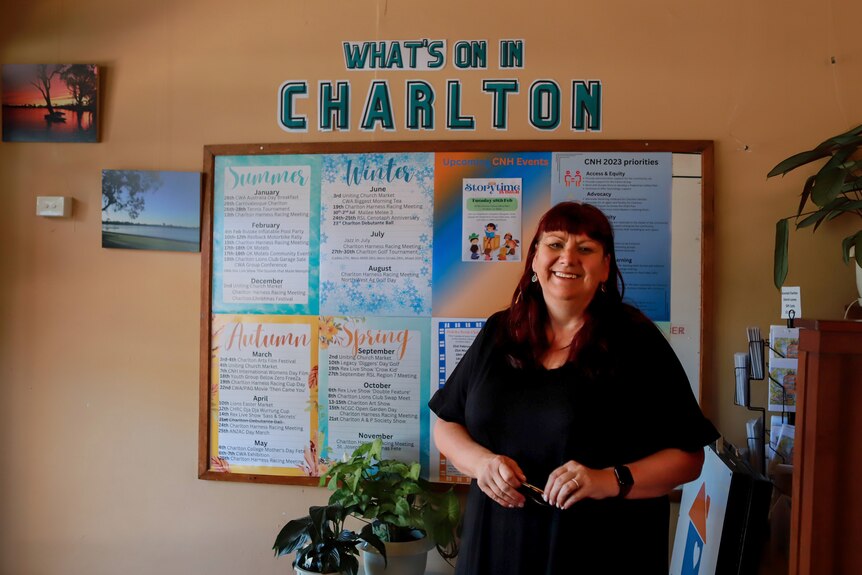 Woman wearing black top smiles standing in front of board with "What's on in Charlton" written above on the wall