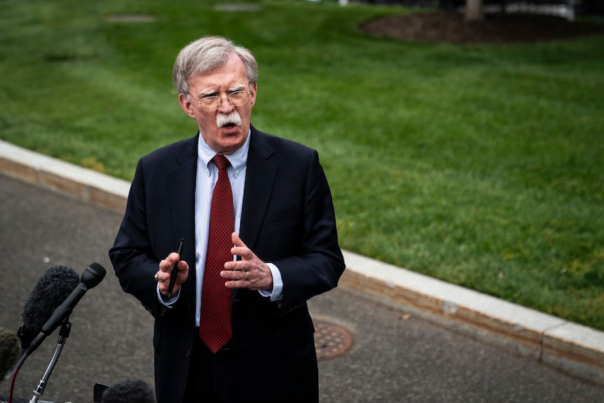 John Bolton speaks to press, he has a stern expression
