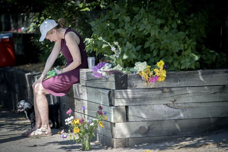 A crying woman sits with her dog surrounded by floral tributes.