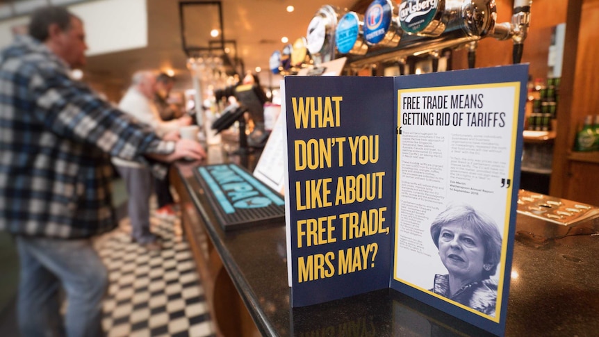 An advertisement aimed at Theresa May sits on a bar in a pub in front of beer taps.