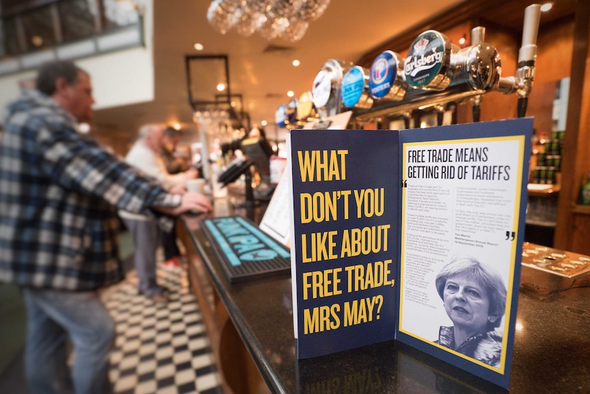 An advertisement aimed at Theresa May sits on a bar in a pub in front of beer taps.