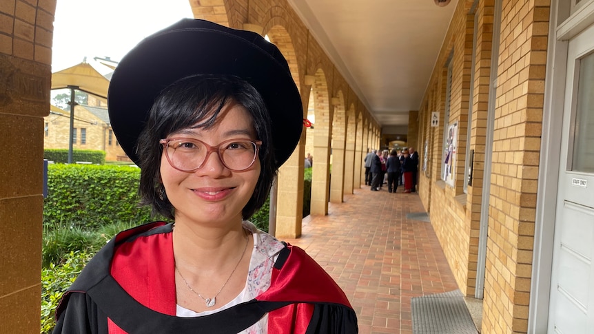 a woman in academic dress wearing glasses smiling at the camera