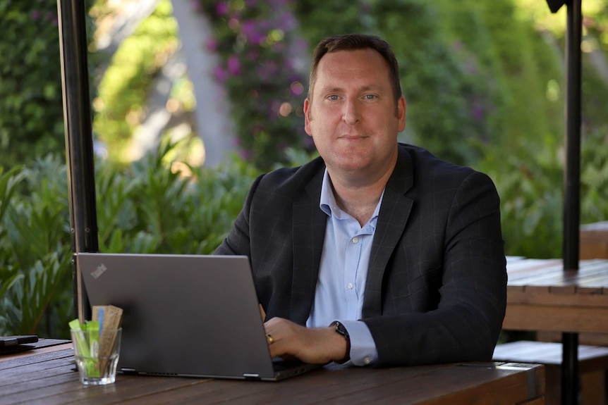 Mr Lacey sits at a table with his laptop.