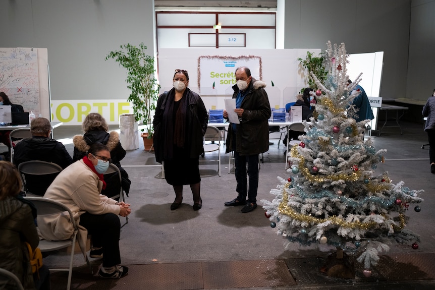 People wait near a Christmas tree during an observation period after being vaccinated