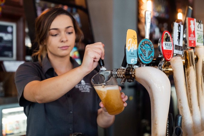 Young female bartender pulls a pint