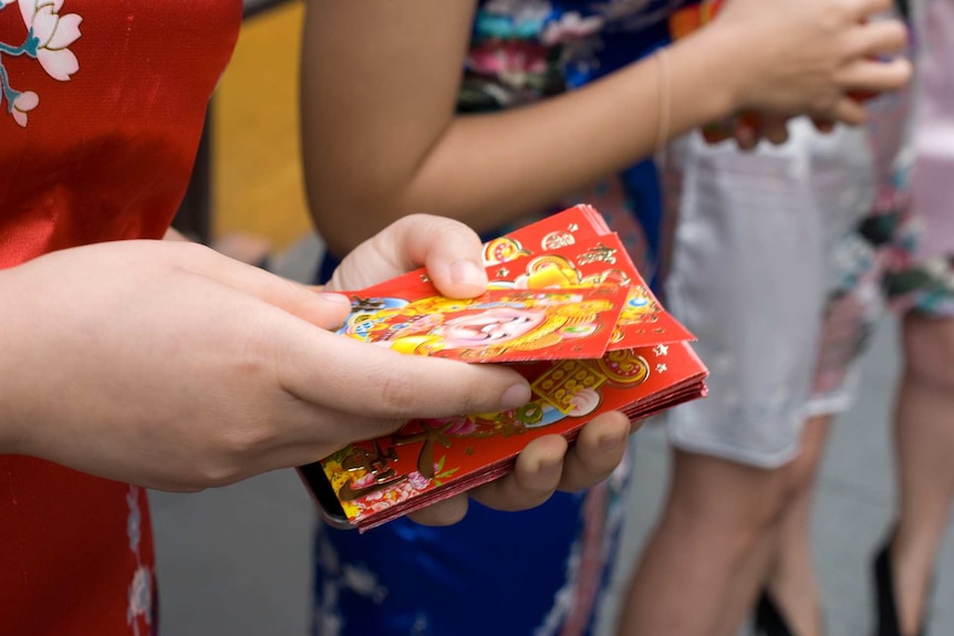 A woman hands out red envelopes.