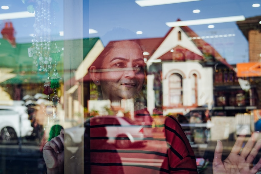 A woman seen through the sheen of a shop window with houses reflected in its front