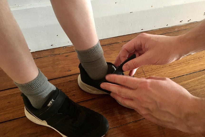 Close-up of a child's feet in shoes and a man tying the laces.