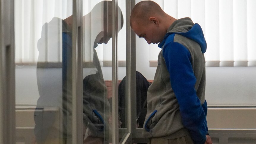 Vadim Shishimarin stands in court during a hearing in Kyiv with his head bowed against a glass barrier