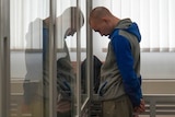 Vadim Shishimarin stands in court during a hearing in Kyiv with his head bowed against a glass barrier