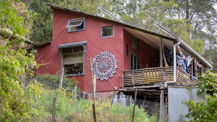 A maroon-coloured, timber-clad home nestled into a bushy hillside.