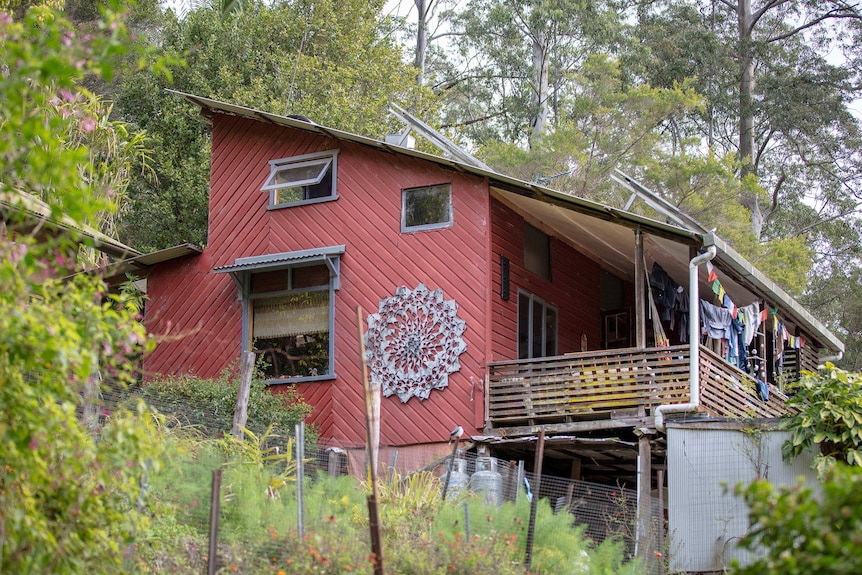 A maroon-coloured, timber-clad home nestled into a bushy hillside.