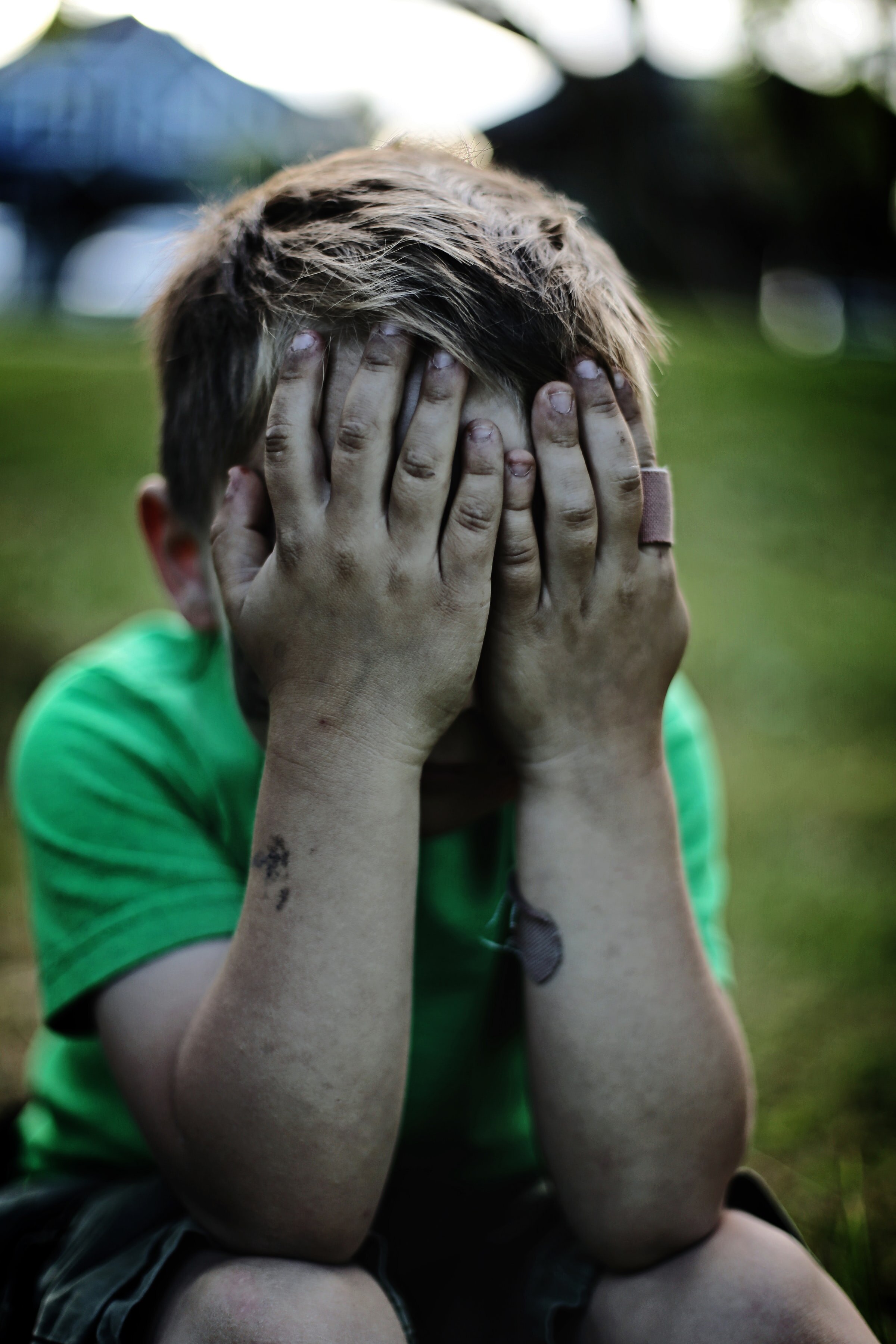A small boy covering his face with both hands while throwing a tantrum.